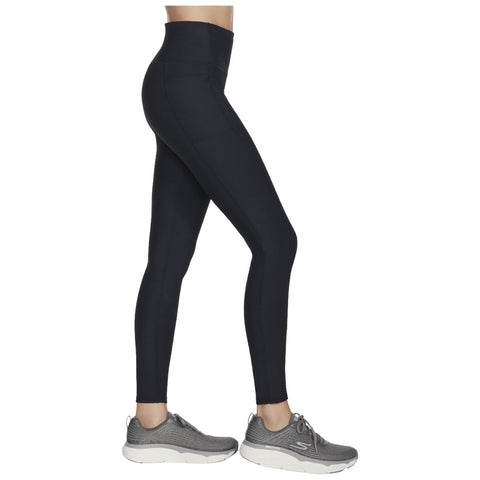 A person is standing sideways wearing high-waisted black leggings and gray athletic shoes with a light sole, showcasing a sporty appearance in a neutral setting.