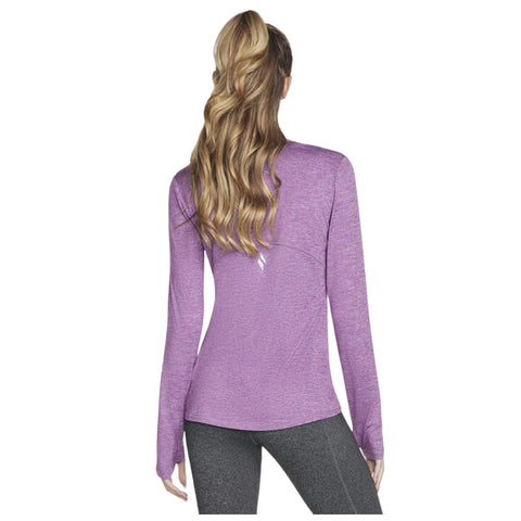 A person with long wavy hair is wearing a purple long-sleeve shirt and black leggings while facing away from the viewer in a neutral background.