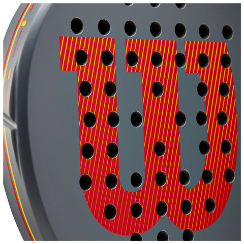 A round object featuring the bold red letters "W" and "U" with diagonal stripes is densely perforated with black holes against a gray background, suggesting a design element or a pattern.