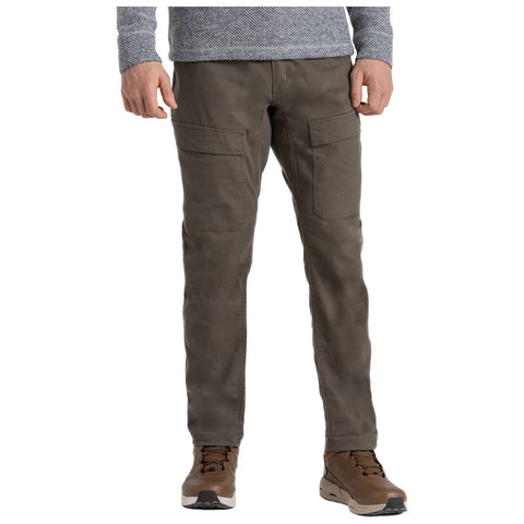 A person stands wearing olive green pants with two large side pockets and brown hiking shoes. They are dressed in a long-sleeve gray patterned shirt, presenting a casual outdoor style.