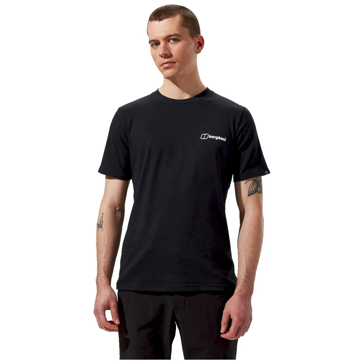 A young man stands confidently wearing a black t-shirt with a small logo on the left chest area in a plain white background setting. His arms are relaxed by his sides.
