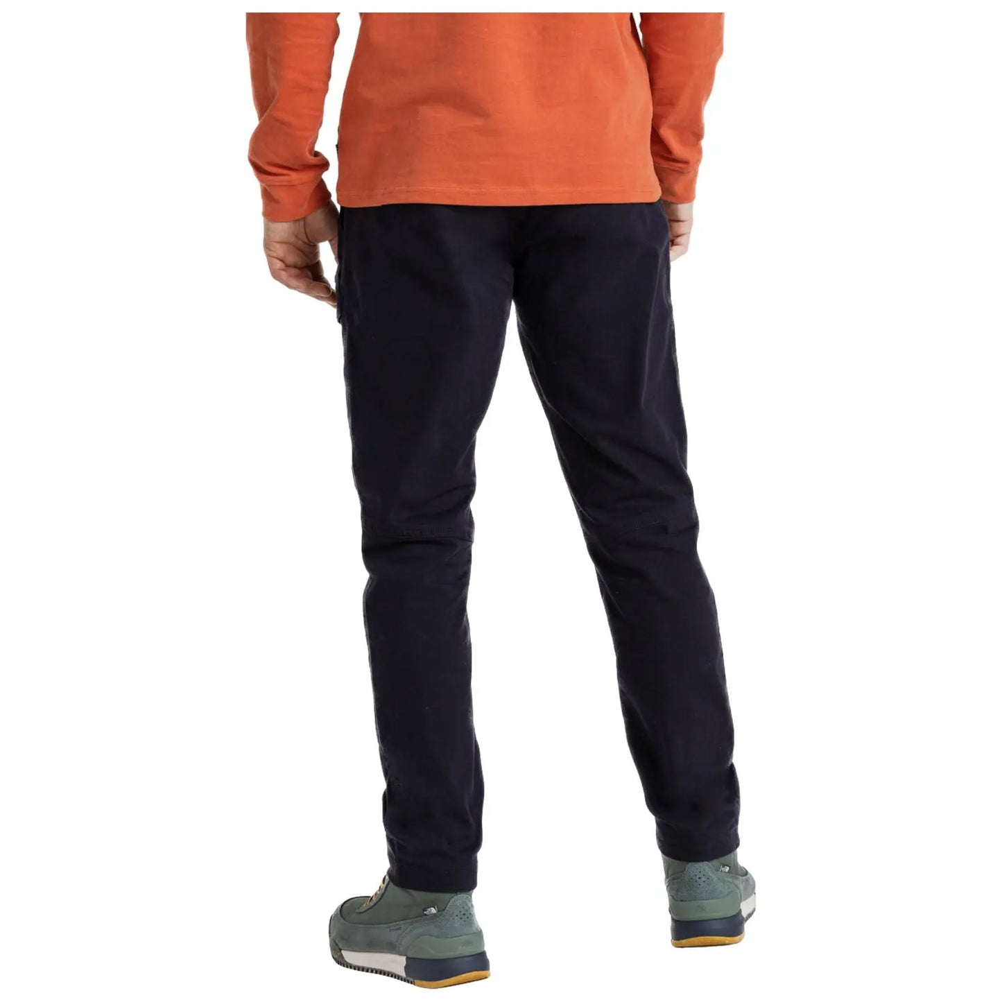 A person stands with their back visible wearing dark pants and green footwear while the upper body is clothed in an orange long-sleeve shirt in a neutral setting