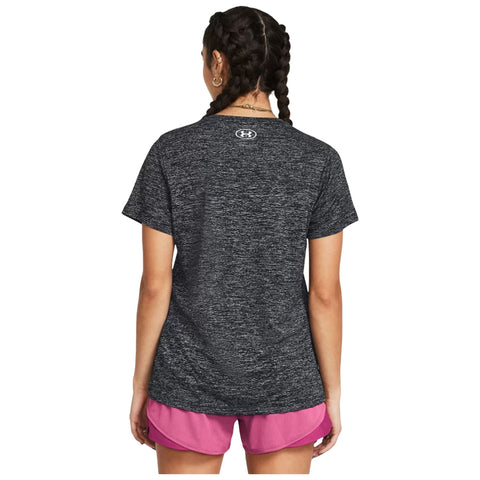 A person stands with their back facing the viewer wearing a black athletic shirt and pink shorts in a neutral setting, likely indoors or against a plain background.