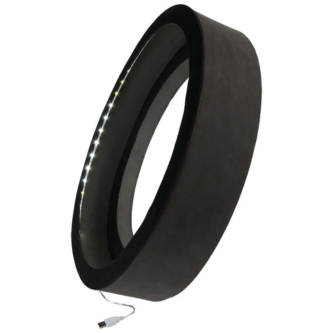 A circular LED lamp with a black exterior emits light from its inner edge while connected to a USB power source suggesting use in a modern interior setting.