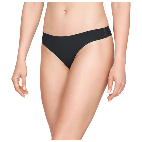 A black thong is being worn by a person standing upright with one hand resting slightly on their thigh and the other hand relaxed by their side in a neutral background.