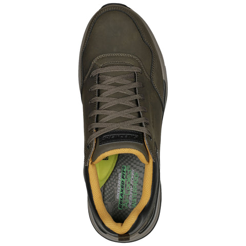 A green shoe is positioned upright with laces tied and a yellow interior lining visible. The context suggests it is a casual or outdoor sneaker, suitable for various activities.