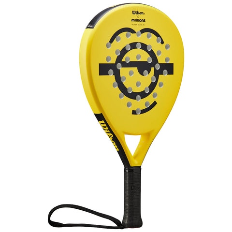 A yellow paddle racket features a smiling face design with circular patterns and a textured black handle. It is used in paddle sports, typically played on a court.