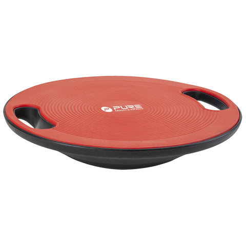 A red and black balance board designed for fitness is positioned horizontally with curved edges and grip handles on each side, ready for use in a home or gym setting.