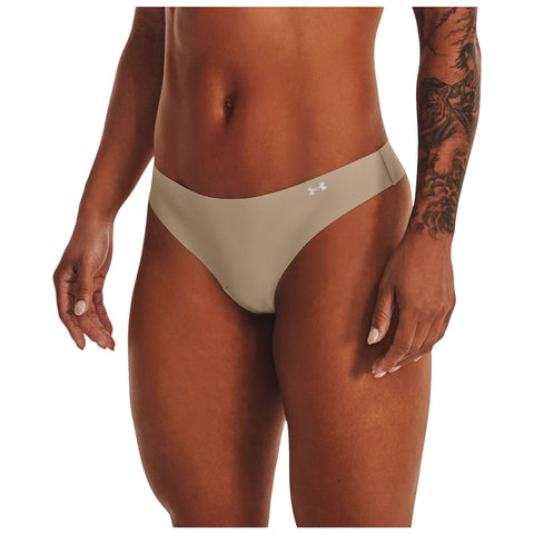 A person is wearing a beige thong bikini bottom that features a small logo. The environment appears neutral with a focus on the swimwear and the visible tattoo on the person's arm.