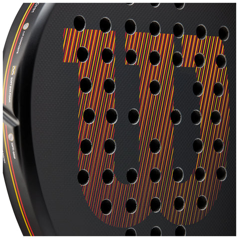 A black paddle with a textured surface features a prominent logo in vibrant colors surrounded by numerous small holes indicating its design for a sport like padel or tennis.