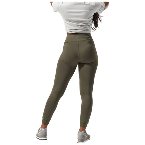A person wears a knotted white top and black leggings while playfully lifting one foot off the ground, showcasing athletic wear in a neutral background.