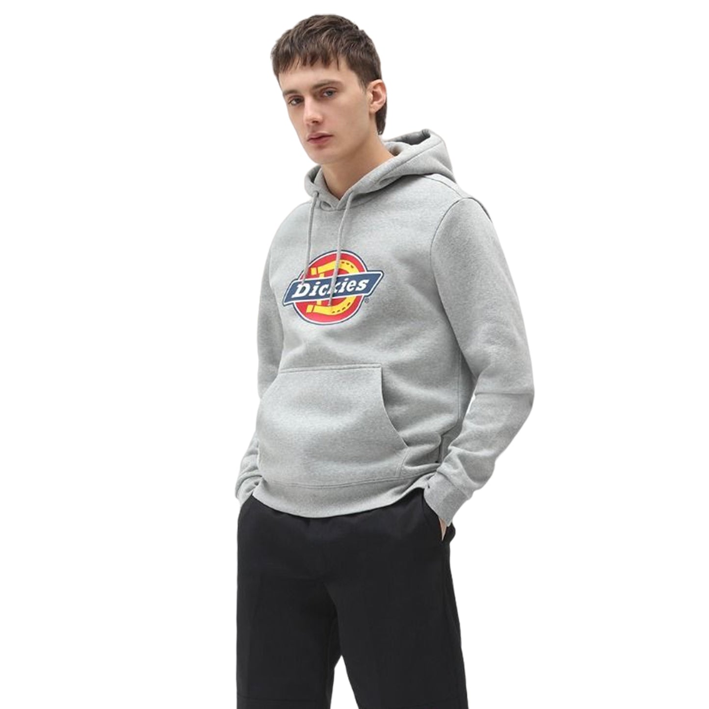 A young man wearing a gray hoodie with a circular logo stands confidently with hands in his pockets against a plain white background.