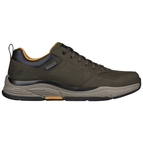 A green waterproof sneaker is displayed with a black heel accent and a tan inner lining while positioned on a flat surface against a plain background.