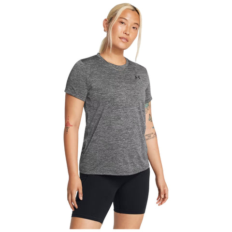 A person stands posing in a fitted gray athletic shirt and black shorts in a neutral background showcasing activewear style and casual confidence.