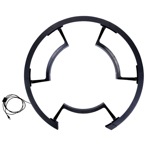 A circular, black plastic frame with gaps is positioned flat, featuring support brackets and a cable attached, potentially designed for holding or connecting equipment in a technical or gaming setup.