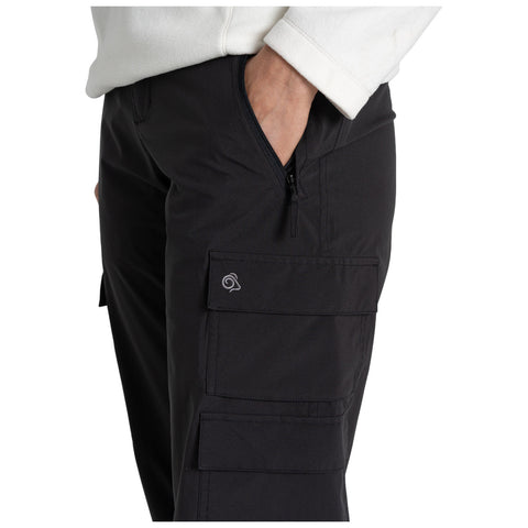 Black cargo pants are being worn with a hand placed in the front zippered pocket featuring multiple side pockets, shown against a neutral background of a white sweatshirt.