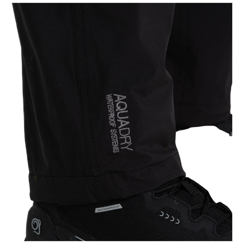 Black waterproof pants are standing next to a waterproof shoe displaying the logo AQUADRY WATERPROOF SYSTEMS highlighting the focus on outdoor gear designed for wet conditions.