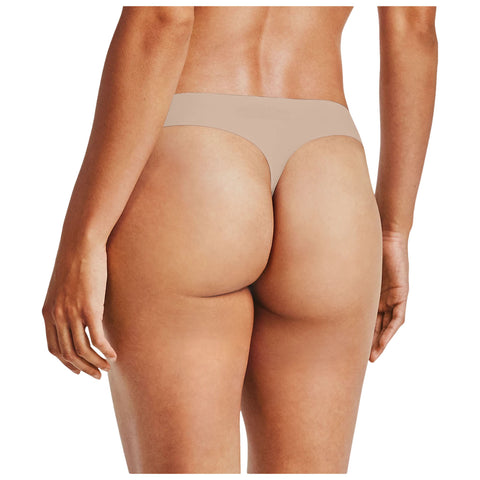 A person stands facing away showing a back view while wearing a nude-colored thong that highlights the curves of their body in a neutral setting