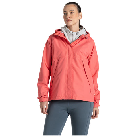 A woman is standing and wearing a bright coral jacket over a light gray hoodie and gray leggings in a neutral background suggesting an active outdoor style.