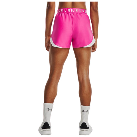 A person stands with their back facing the viewer wearing bright pink athletic shorts with a white trim and white socks paired with black and white sneakers in an outdoor or gym setting.