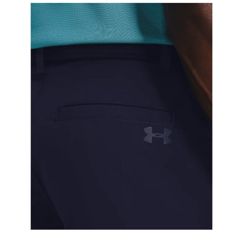 A pair of dark navy pants is prominently displayed with a small pocket on the back and an understated Under Armour logo near the waistband, set against a contrasting turquoise top.
