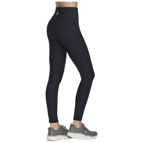 Black leggings with a high waistband are being worn by a person standing sideways. They are paired with grey athletic shoes. The setting is neutral without visible background details.
