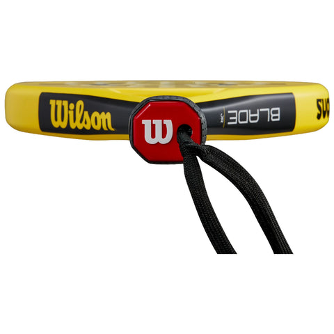 A yellow tennis racket with a black and red grip is displayed horizontally showing the brand name Wilson prominently alongside the string pattern and grip details in a plain background.