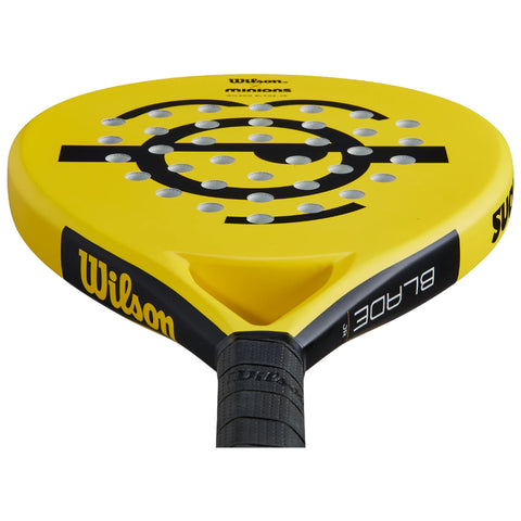 A bright yellow paddle with a circular head features multiple holes for striking. The paddle is oriented towards the viewer against a neutral background, indicating readiness for play.