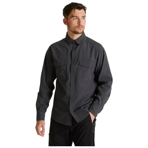 A man stands wearing a dark gray button-up shirt with two front pockets looking slightly off-camera in a plain background. He appears to have a neutral expression.