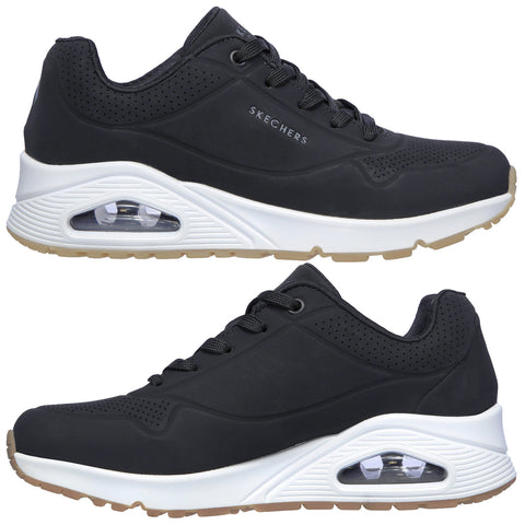 A black athletic shoe featuring a mesh upper and memory foam insole sits on a light background with a textured rubber sole showing patterns for traction