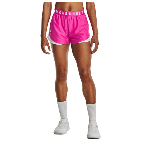 Pink athletic shorts are worn by a person standing upright wearing white shoes and socks with the waistband displaying the text ARMOUR UNDER. The context is a casual or sporty setting.