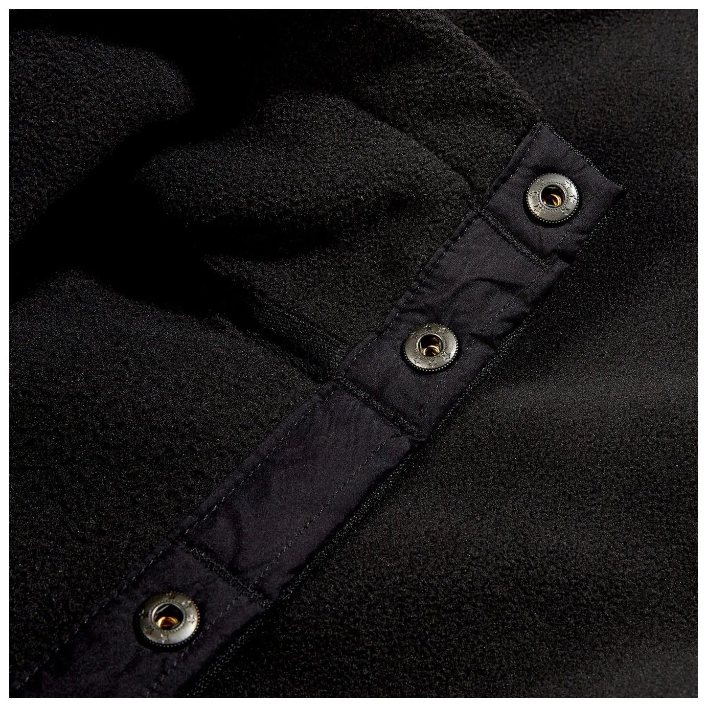A close-up of a black fleece fabric featuring a button closure with metallic snaps the material appears soft and has a textured surface against a dark background.