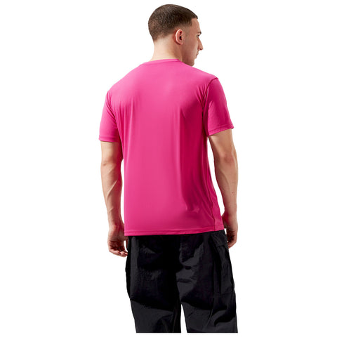 A person stands with their back facing the viewer wearing a bright pink short-sleeved shirt and black pants in a neutral background setting