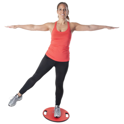 A woman in a red tank top and black leggings stands on a balance board with one leg raised and arms extended for balance in a neutral background.