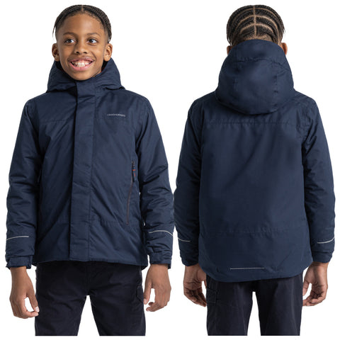 A young boy wearing a navy blue jacket is smiling while facing forward. His braided hair is visible. The setting is neutral and focused on the boy and his clothing.