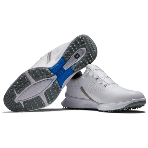 White athletic shoes are displayed with their soles facing upward showcasing a patterned grip featuring small studs The setting is neutral emphasizing the shoe design and features.