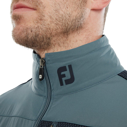 A man is wearing a gray high-collared jacket with a zip and an FJ logo on the collar, showcasing a close-up of his chin and jaw, with a neutral background.