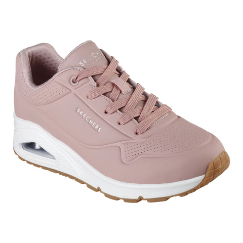 A pink sneaker with a smooth surface features lace-up design and a cushioned heel. It shows branding on the side and has a white sole with a textured gum rubber bottom.