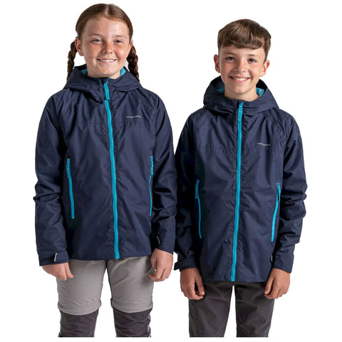Two children are standing side by side wearing matching dark jackets with bright blue zippers. They are smiling directly at the viewer in a neutral setting.