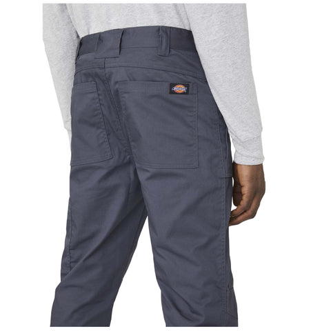 A person stands wearing gray long sleeves and dark gray pants with two back pockets showcasing a label on the waistband the setting is neutral and focused on the clothing details.