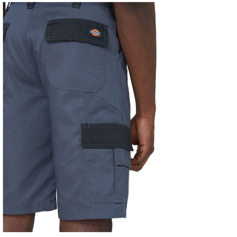 Gray cargo shorts are displayed from the side showcasing multiple pockets and contrasting black patches the wearer has a hand resting near the waistband suggesting an active stance or readiness