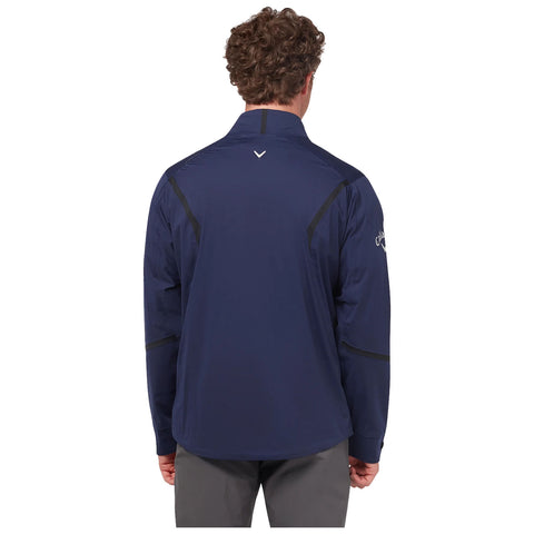 A man is standing with his back turned wearing a navy jacket with black accents in a neutral setting. The jacket features a collar and appears lightweight and sporty.
