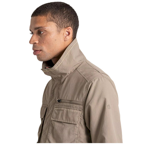 A man wearing a light brown jacket with a high collar stands in profile highlighting the jacket's zippered pocket and casual design against a plain white background.