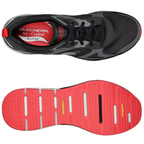 Black athletic shoe with red accents is positioned upright showing the top view and underside. The shoe features mesh material and a cushioning sole designed for support and comfort.