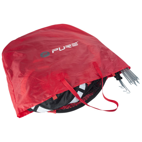 A red storage bag containing a folded item is shown with several metal stakes protruding from the side indicating it is meant for outdoor use or setup.