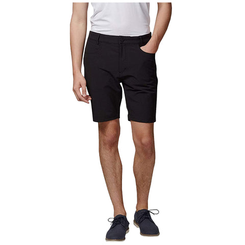 A person stands wearing black shorts and a white shirt with one hand in their pocket while wearing dark shoes in a neutral setting.