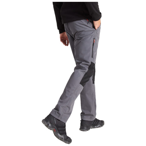 A person wearing gray outdoor pants and black hiking shoes is walking, with their right hand in a pocket and the left hand relaxed, in a natural outdoor setting.