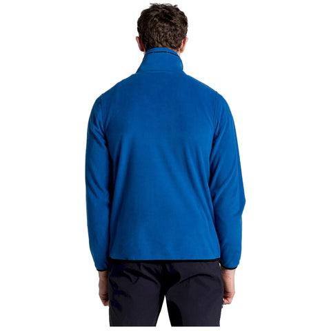 A person is standing with their back facing the viewer wearing a bright blue fleece jacket and black pants in a plain white background.