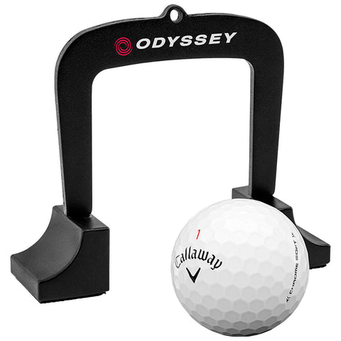 A black golf alignment guide stands upright above a white Callaway golf ball marked with the number one positioned on a flat surface, indicating preparation for a shot during practice.