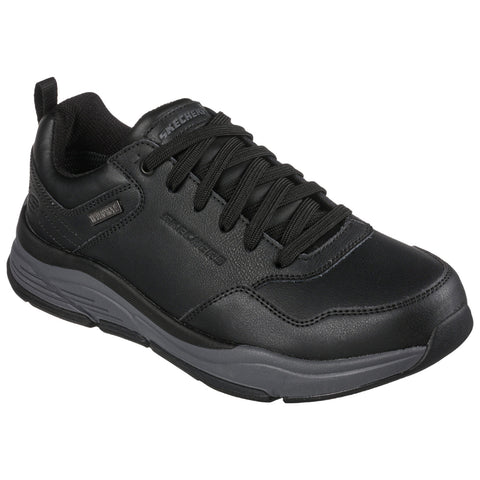 A black sneaker with a textured leather design features green laces and a sturdy sole displayed against a neutral background emphasizing its sporty and casual style.